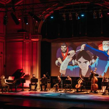 En la foto se enfoca el escenario del Aula Magna con nueve músicos y músicas interpretando el concierto sobre la música popular del Studio Ghibli.