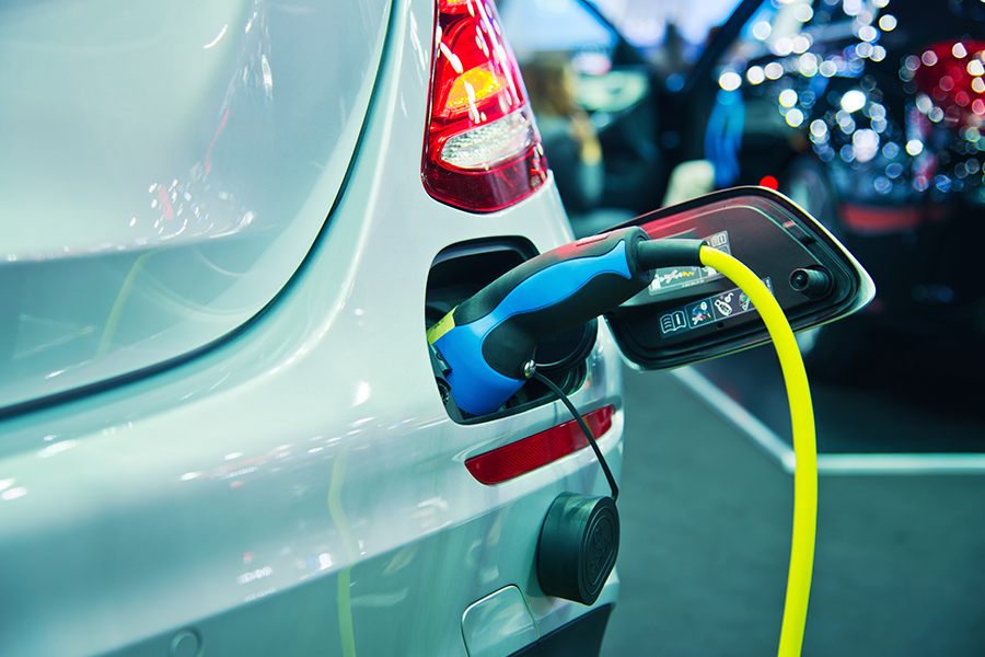 Close-up of the rear of a silver electric vehicle that is plugged in and charging.