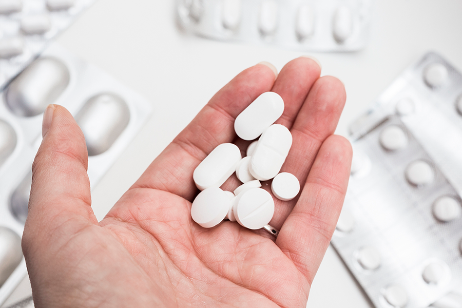 Primeiro plano de uma mão aberta segurando um punhado de comprimidos brancos sobre um fundo de blisters.
