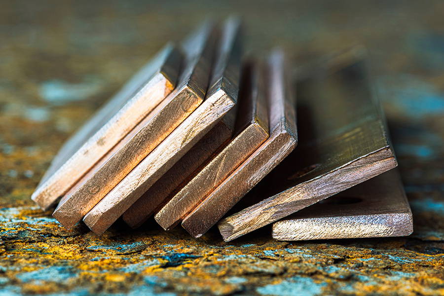 A close-up shows a pile of shiny rectangular copper bars stacked on a rough, rusty surface.