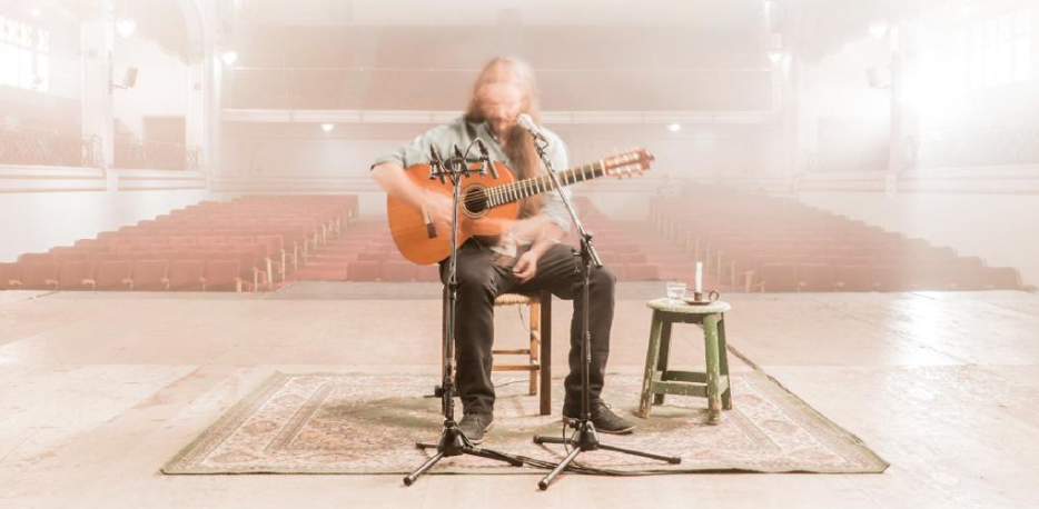 Imagen referente a la actividad, donde se ve en un escenario con una persona con su guitarra y al fondo sillas vacías
