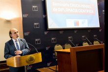 Rector Vidal exponiendo sobre podium del gobierno. Fondo azul y pantalla informativa