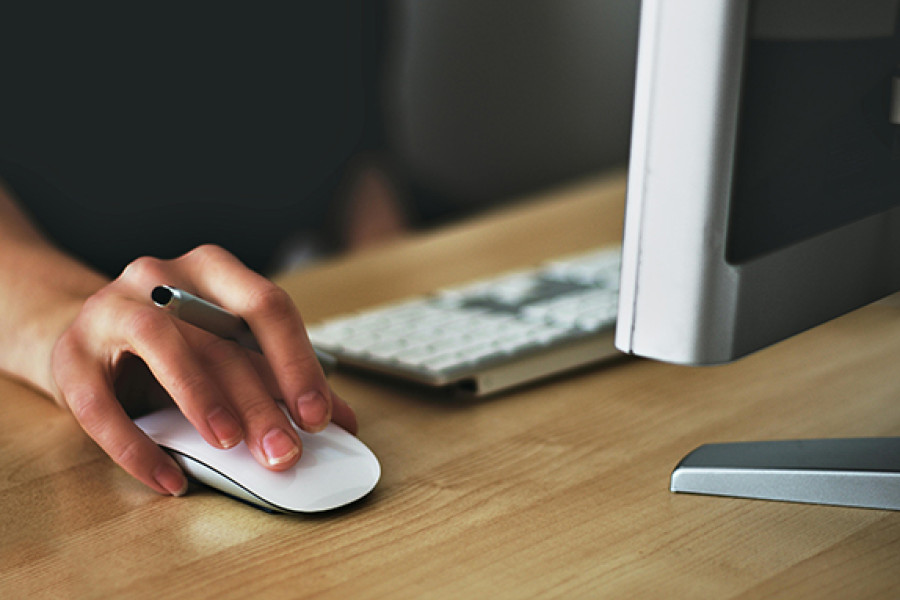 The image shows the screen and keyboard of a computer on a desk and a hand on the mouse.