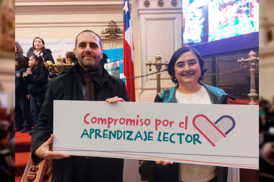 Dos personas sostienen un cartón con letras que dicen "Compromiso con el aprendizaje lector"