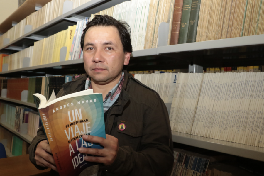 Dr. Andrés Navas aparece en la fotografía con un libro en la mano. En el fondo se puede observar algunos anaqueles de una biblioteca