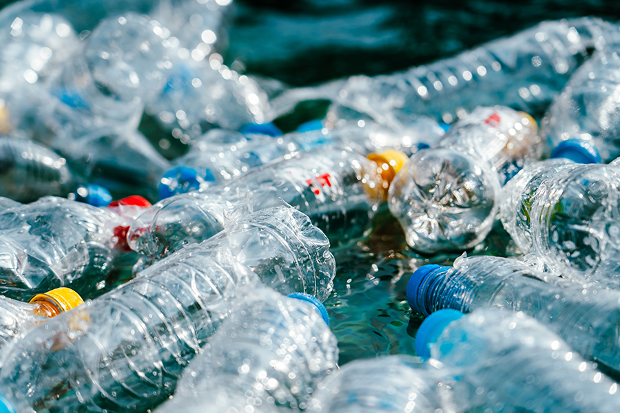 A dense collection of clear, discarded plastic water bottles with colorful caps is seen floating in teal-colored water.