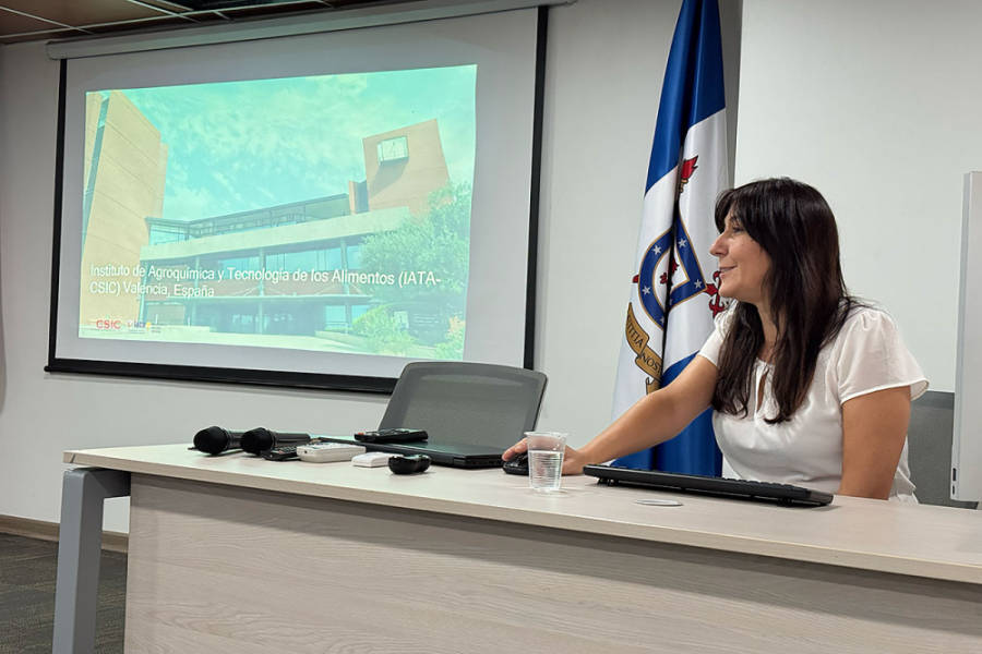 En la fotografía aparece la científica española Dra. Amparo Tárrega, experta en percepción sensorial y hábitos alimentarios en personas mayores, dirigiéndose a la asistencia. Ella aparece sentada en una mesa-estrado. De fondo su presentación. 