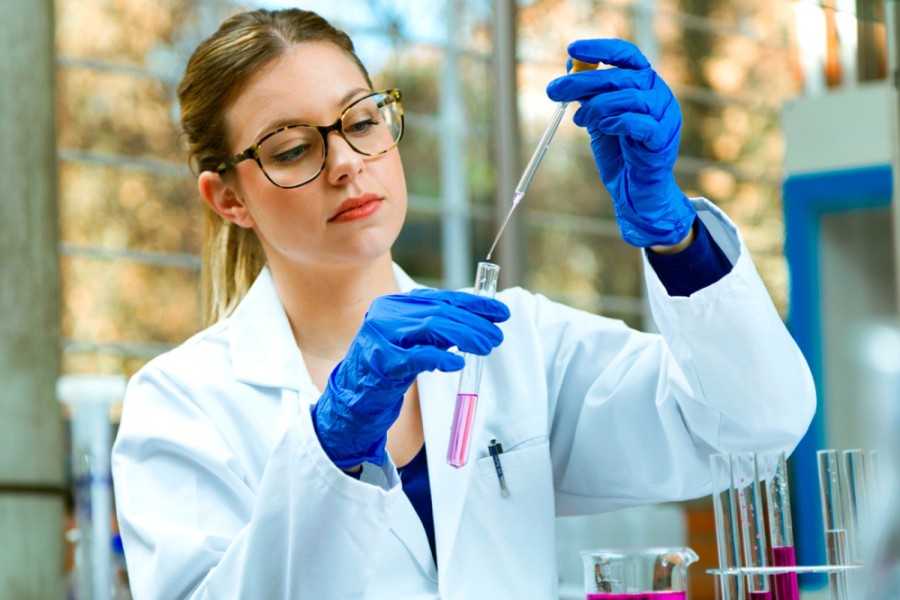 En la fotografía aparece una científica manipulando instrumentos en un laboratorio. ella lleva un delantal blanco y guantes de goma color azul.