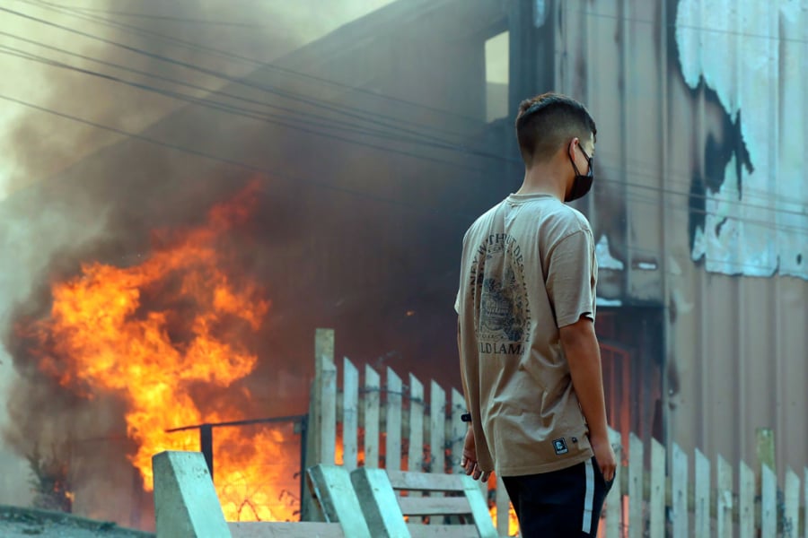 En la imagen aparece un joven mirando como se quema una casa e intentando salvar lo posible.