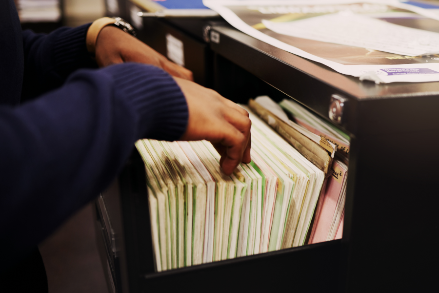 Manos revisando un cajón con carpetas de archivos ordenadas.