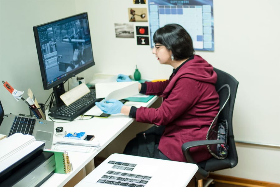 La imagen muestra a una mujer manipulando documentos frente a un computador