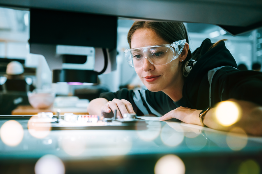 Woman wearing safety glasses looking closely at a glowing, illuminated glass workspace.
