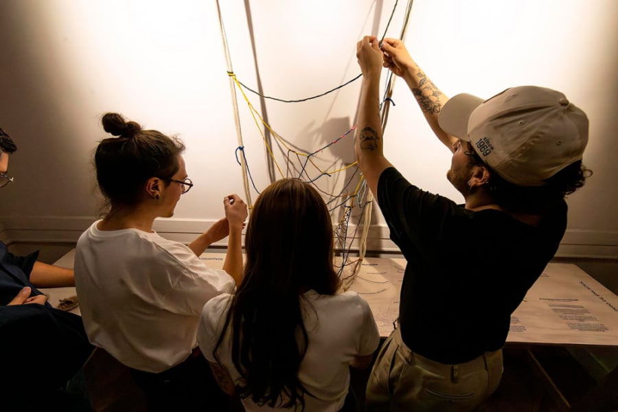 La imagen muestra a dos mujeres y un hombre explorando una de las obras textiles de la exposición