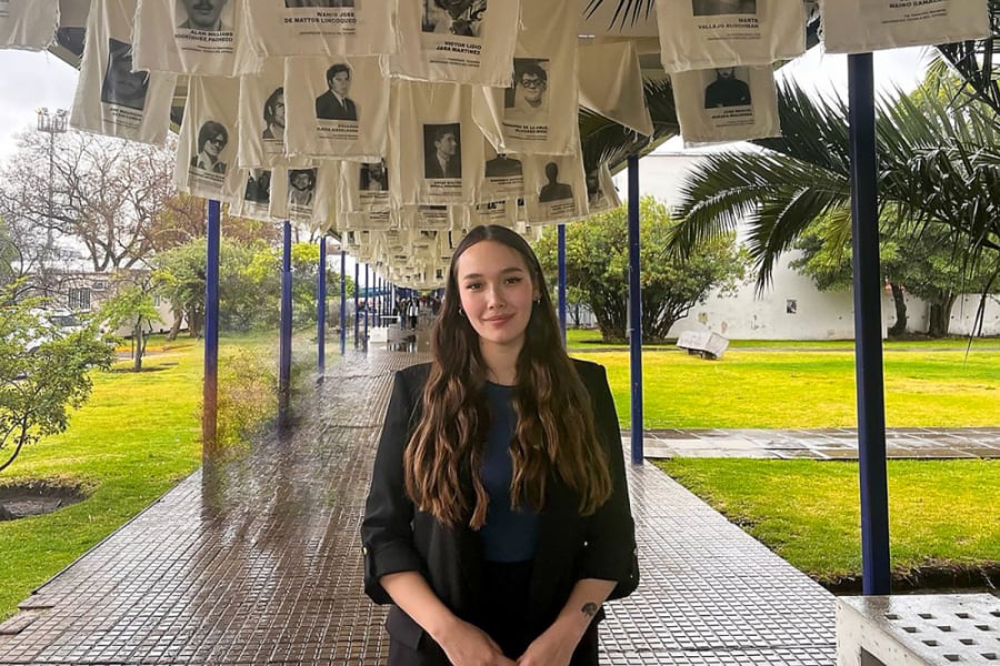 La imagen muestra a la egresada posando frente a la cámara, en uno de los pasillos de la universidad