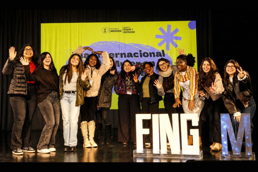 En la imagen aparecen una docena de estudiantes que posan a la cámara en el escenario central de la actividad con unas letras grandes que indican FING M que se refiere a Facultad de Ingeniería Mujeres
