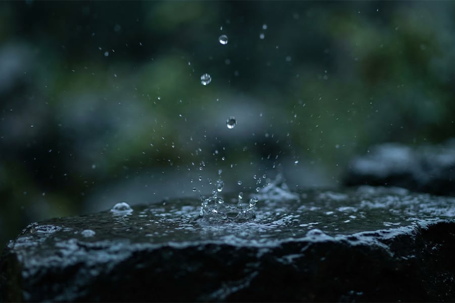 Water drops splashing onto a wet dark stone during rainfall.