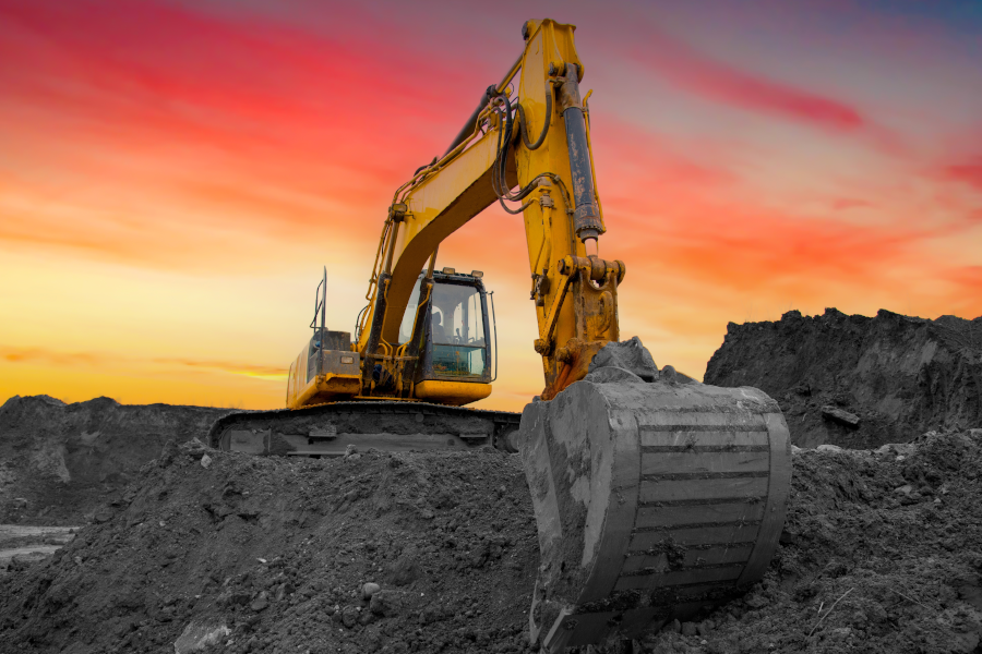 Una excavadora amarilla cavando tierra bajo un cielo de atardecer intenso.