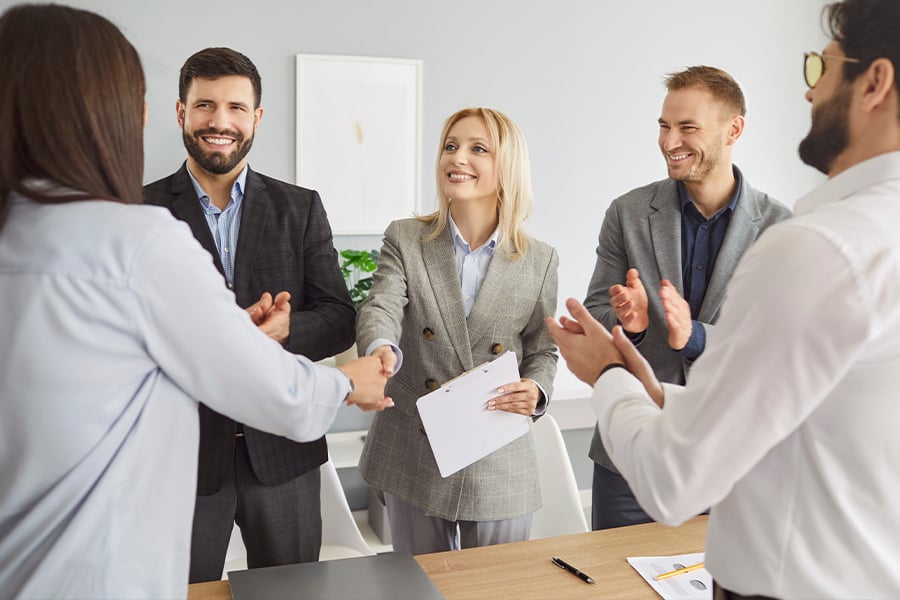 Empresarios dándose la mano y aplaudiendo alrededor de una mesa de reuniones.