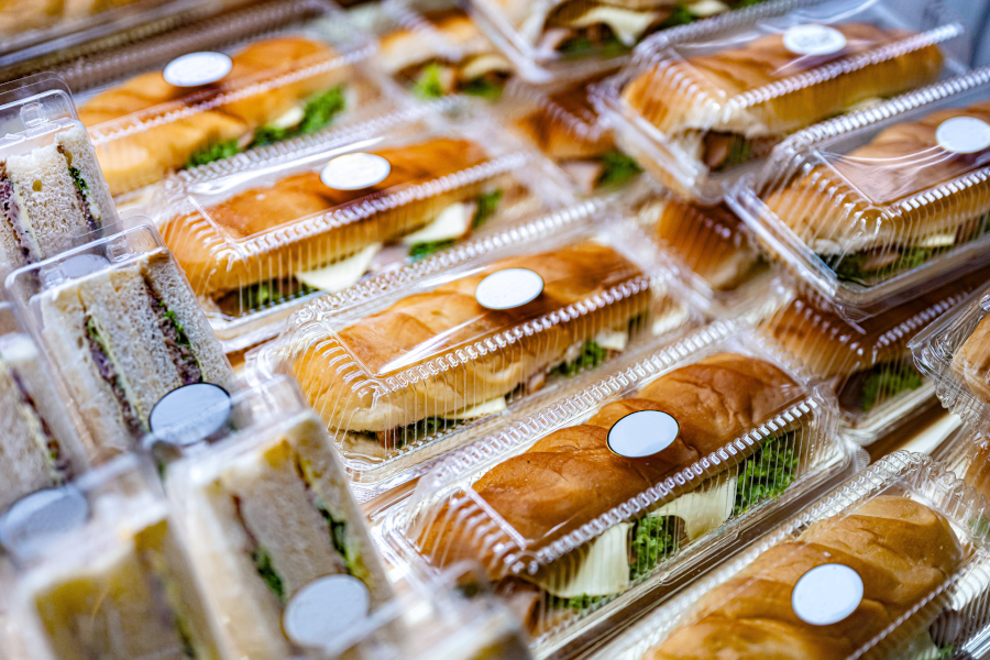 Sándwiches y baguettes envasados en recipientes de plástico transparente en una vitrina.
