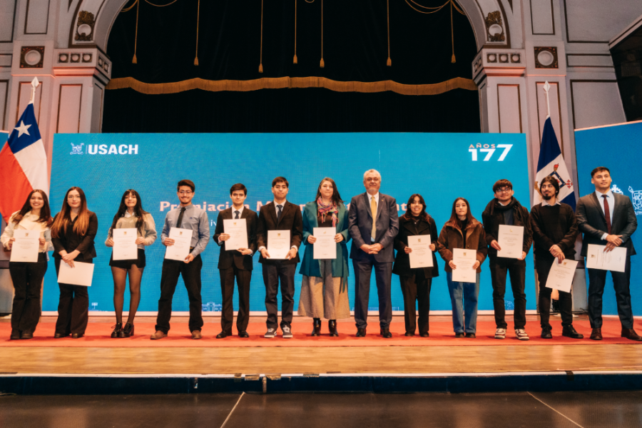 La foto muestra a las y los estudiantes distinguidos durante la ceremonia, posando con sus diplomas junto al rector en el escenario del Aula Magna