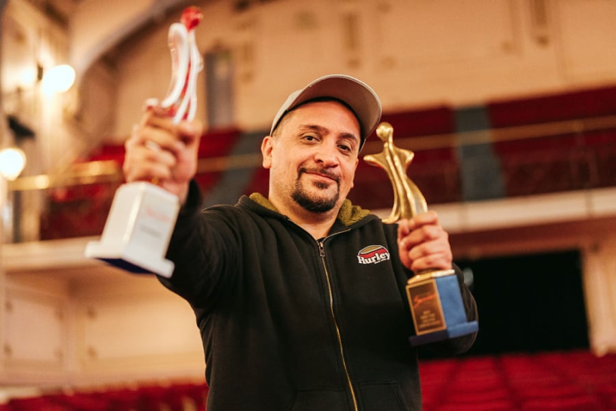 La foto muestra al director con sus dos premios en la mano, posando en el Aula Magna de la Usach