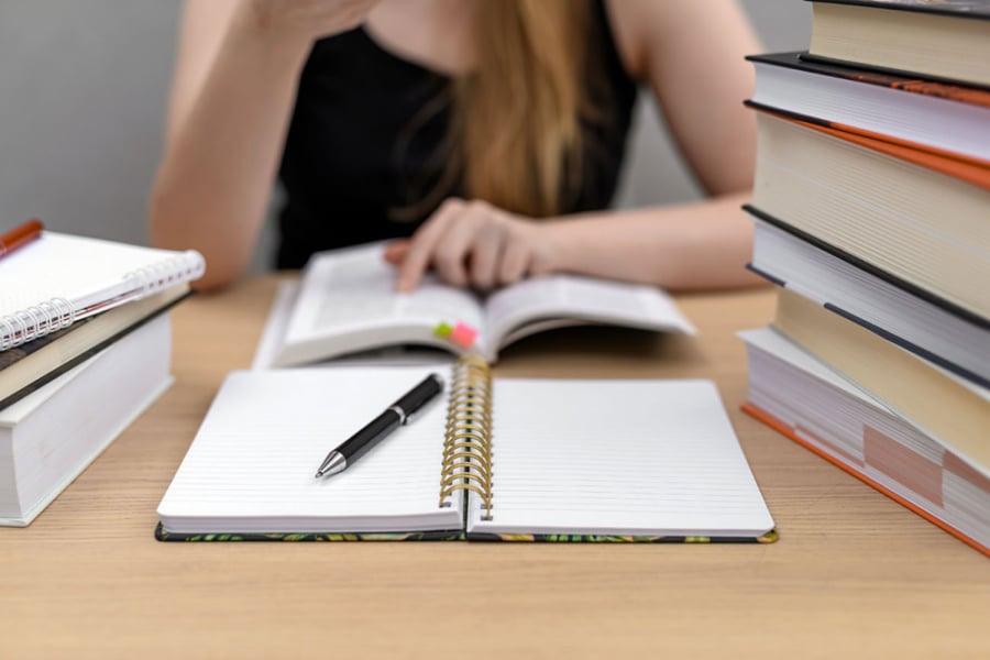 En la imagen aparece una joven estudiante con artículos como cuaderns, lápices en modo estudio.