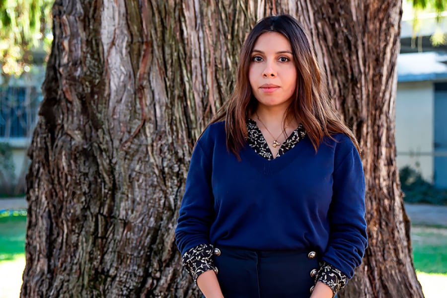 La foto muestra a la investigadora posando de pie frente a un árbol de la universidad
