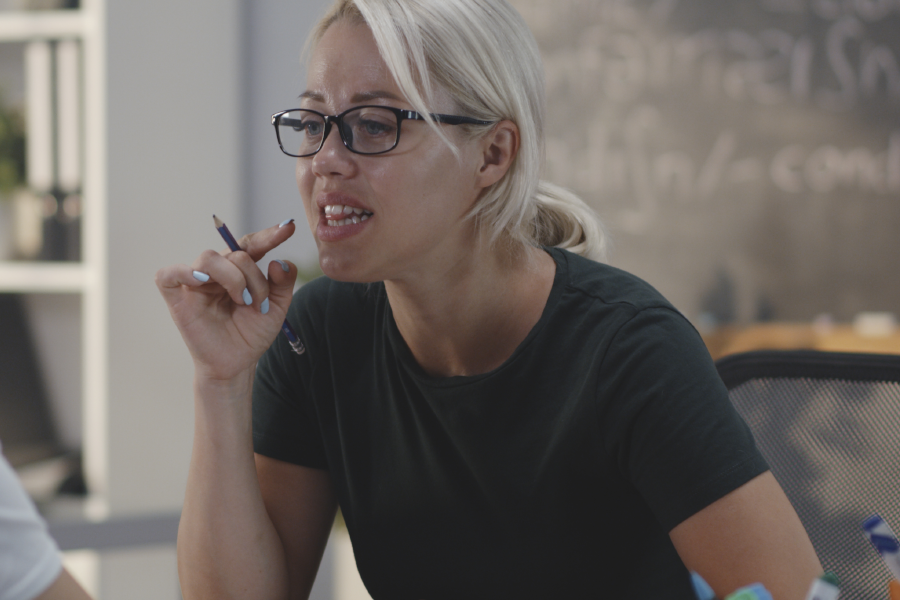 Woman talking dynamically while holding a pencil in a classroom.