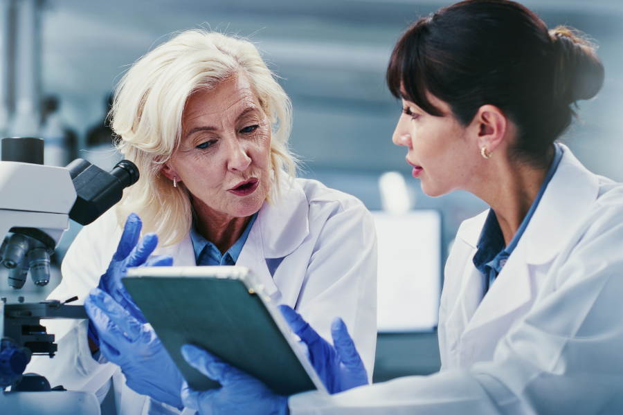 Two scientists in lab coats discussing data on a tablet.