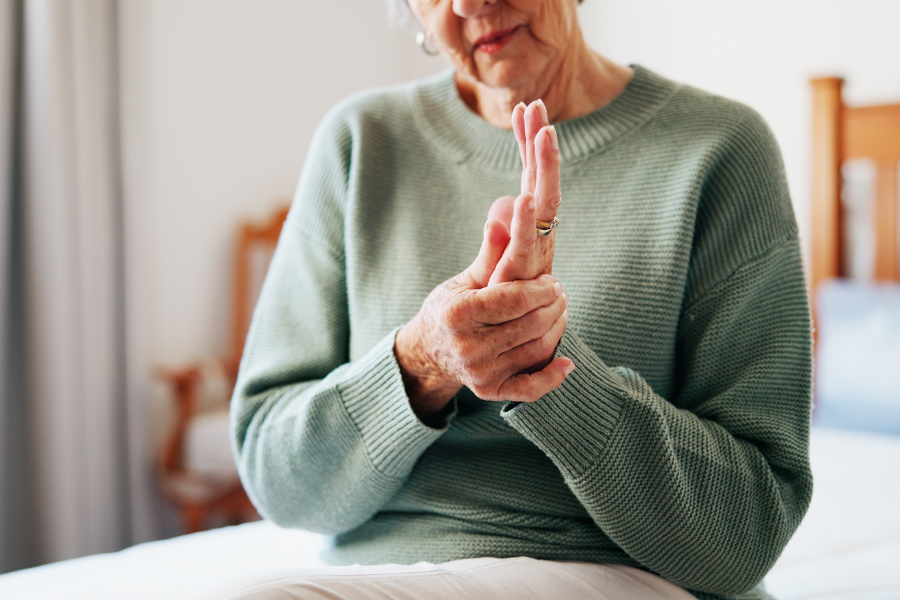 Elderly woman gently massaging her trembling hand while sitting down.