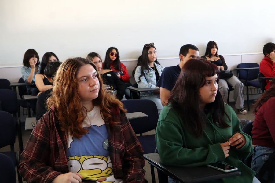 La foto muestra a estudiantes sentados mientras escuchan una clase