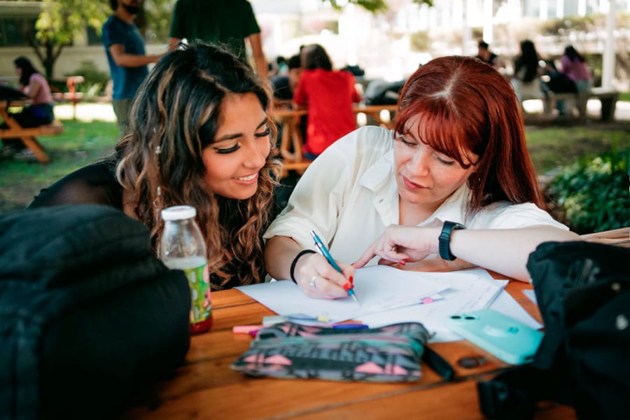 En la imagen aparecen dos jóvenes estudiando en los patios de la universidad