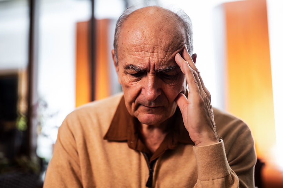 An elderly man holds his forehead, looking anxious and tired.